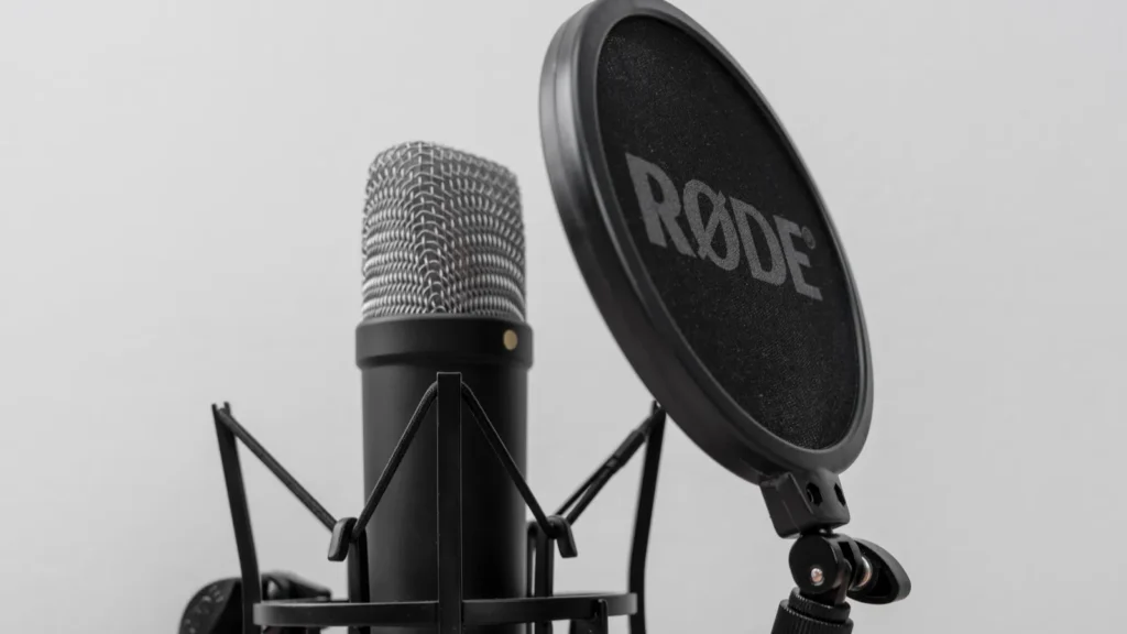 Bar Montenegro February 6 2026 Black studio condenser microphone RODE in shock mount with pop filter on wooden desk against gray wall background closeup audio recording setup with metal grille