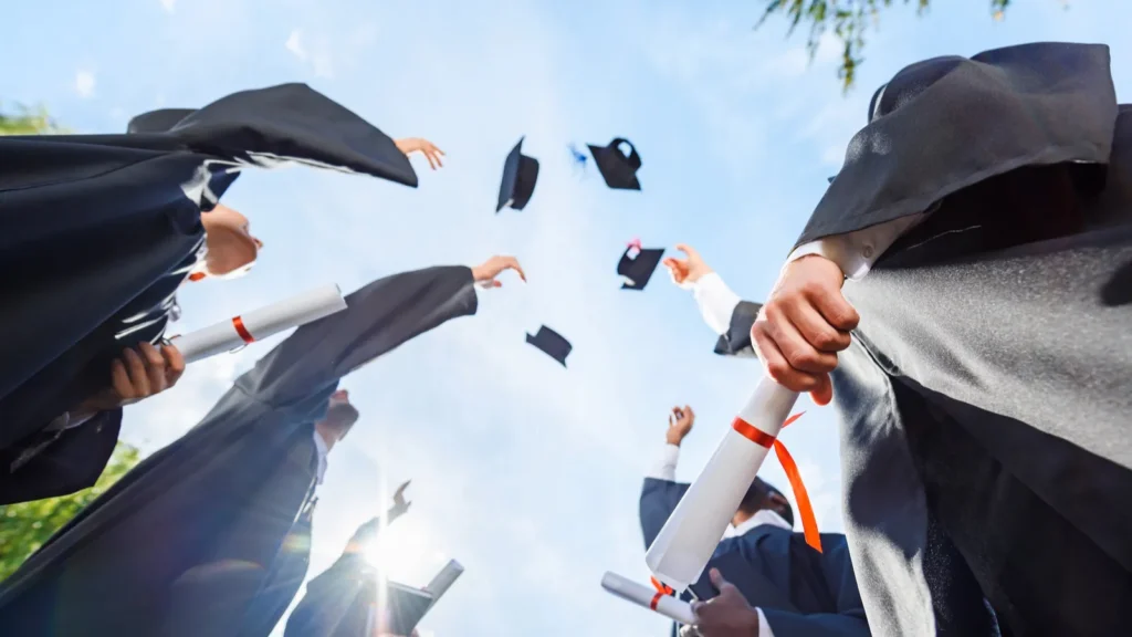 bottom view of graduated students throwing up hats in front of blue sky
