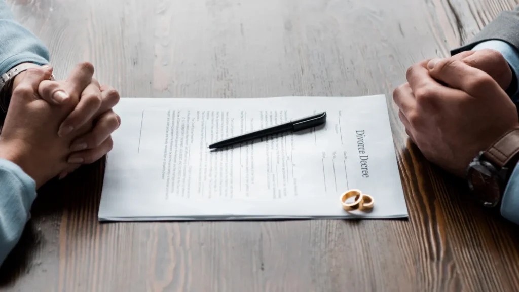 Divorce decree document with wedding rings and a pen on a wooden table.