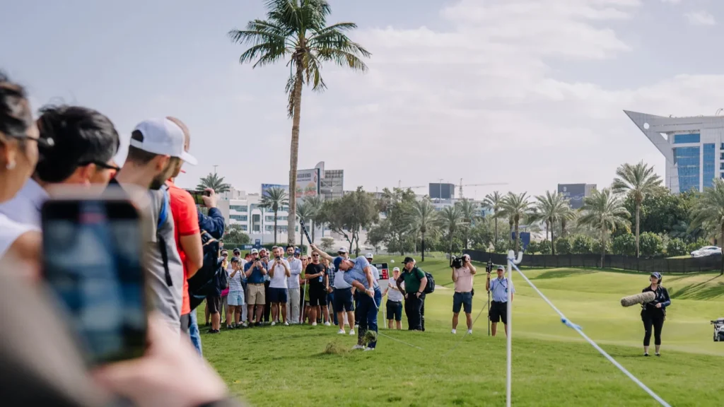 Dubai United Arab Emirates  January 16 2026 Crowd at a golf tournament watches a player on the green with palm trees and modern buildings visible