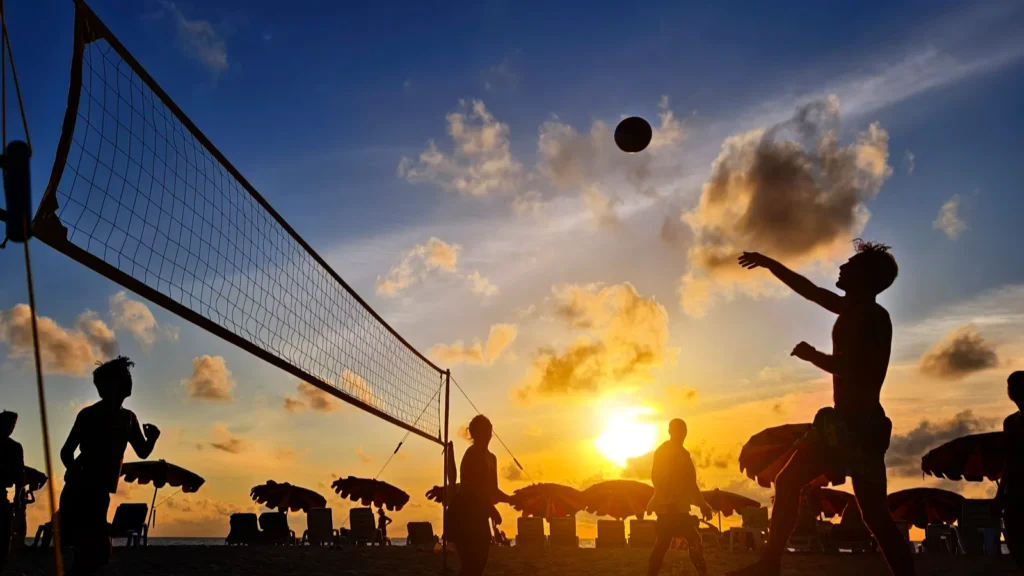 Young people playing beach volleyball by the ocean at sunset