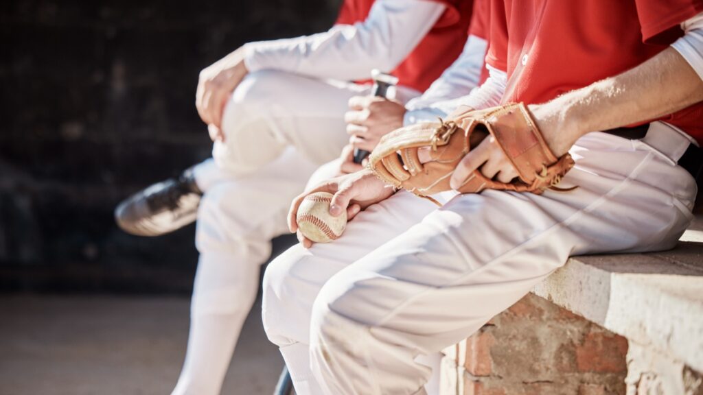 Baseball players in white pants and red jerseys sitting on a bench with a glove and ball.