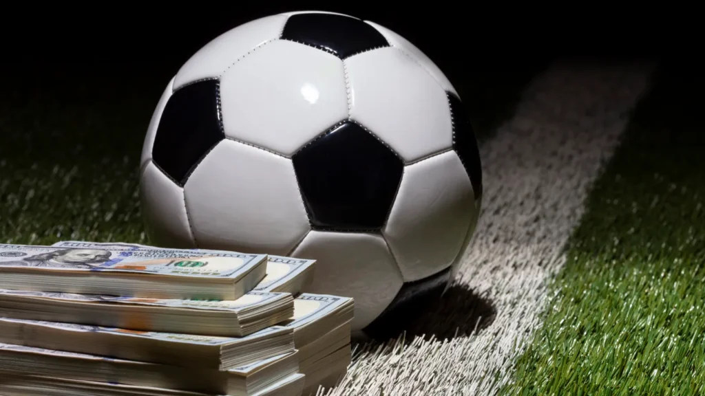 A soccer ball on a grass field with stacks of $100 bills next to it.