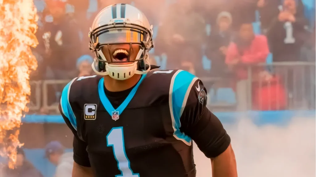 Panthers quarterback wearing jersey number 1 with helmet, celebrating as flames shoot up the sideline and fans cheer in the background.