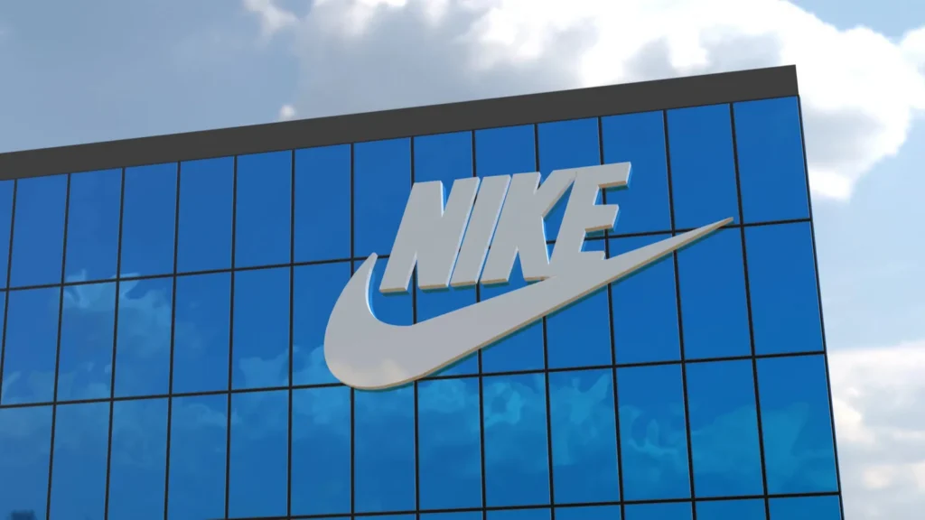 Nike logo and swoosh displayed on a blue glass building exterior against a cloudy sky.