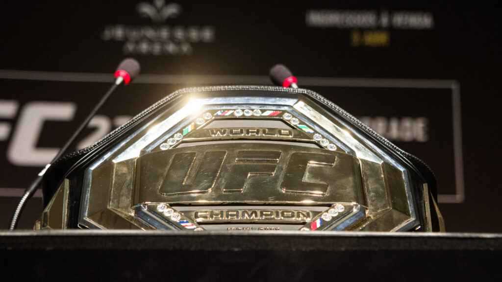 UFC World Championship belt displayed on a podium with two microphones nearby on a press stage.