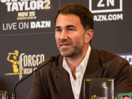 Eddie Hearn speaking into a microphone at a press conference, with a DAZN-branded backdrop behind him