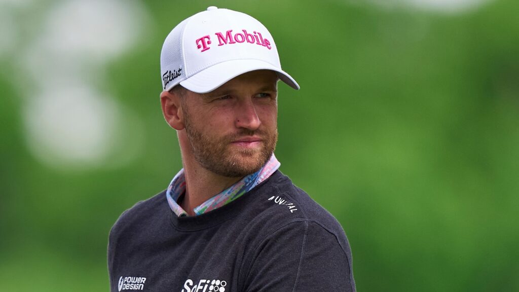 Man outdoors wearing a white T-Mobile cap and dark sweatshirt, looking to the right, with a green blurred background.