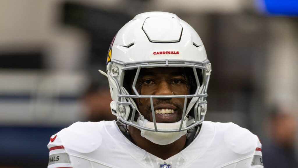 Close-up of a football player in a white Cardinals helmet, face visible through the faceguard and smiling.