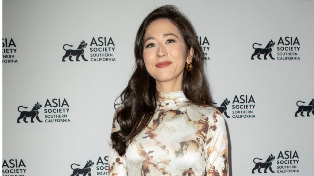 Woman with long dark hair and a marble-patterned blouse smiles at the camera in front of an Asia Society backdrop.