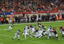 NFL players battle for yardage during a crowded football game as fans watch from the stands.