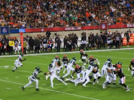 NFL players battle for yardage during a crowded football game as fans watch from the stands.