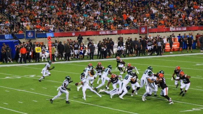 NFL players battle for yardage during a crowded football game as fans watch from the stands.