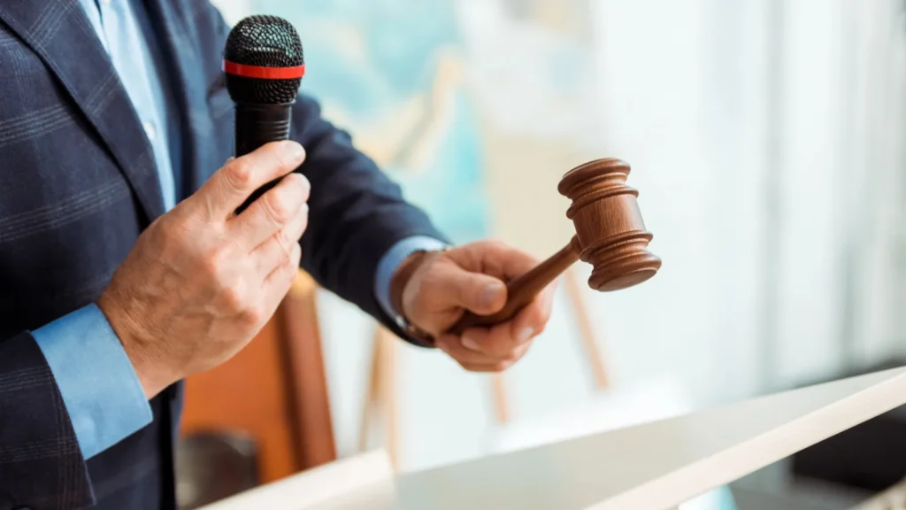 cropped view of auctioneer in suit talking with microphone and