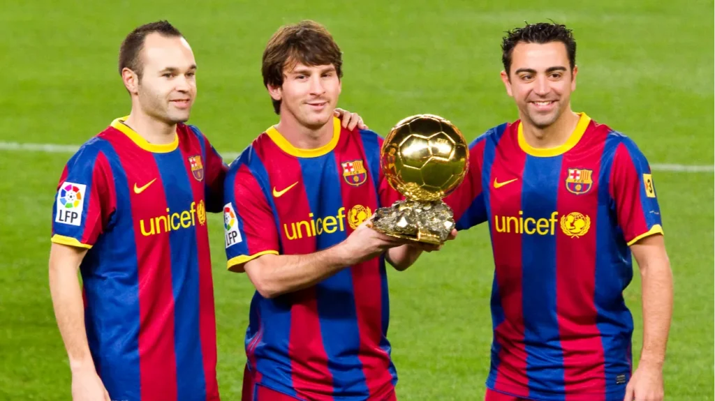Lionel Messi holding a Ballon d'Or trophy alongside his FC Barcelona teammates Andrés Iniesta (left) and Xavi Hernández (right)