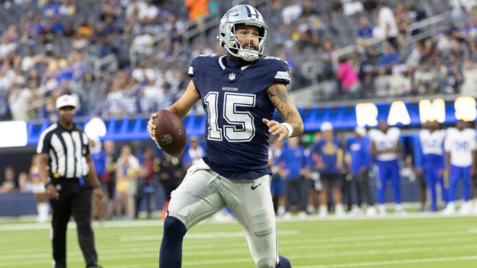 Dallas Cowboys quarterback Will Grier Dallas Cowboys football player wearing #15 runs with the ball during a game on the field while fans watch in the stands.