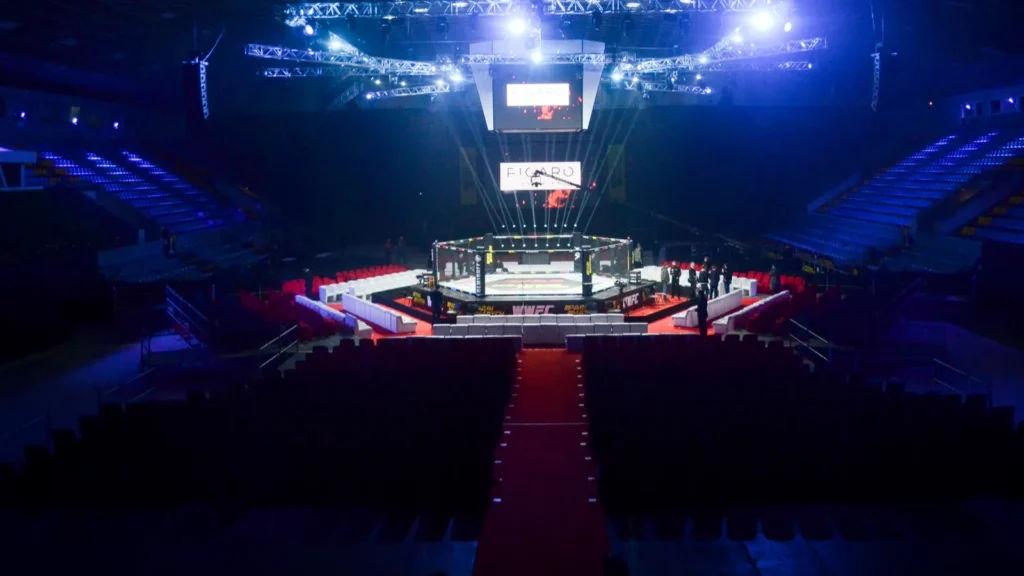 An empty fighting octagon in a dimly lit arena.