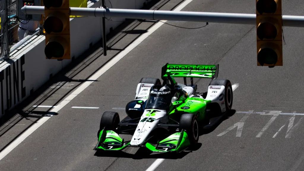 IndyCar racing down a city street circuit past an overhead traffic light.