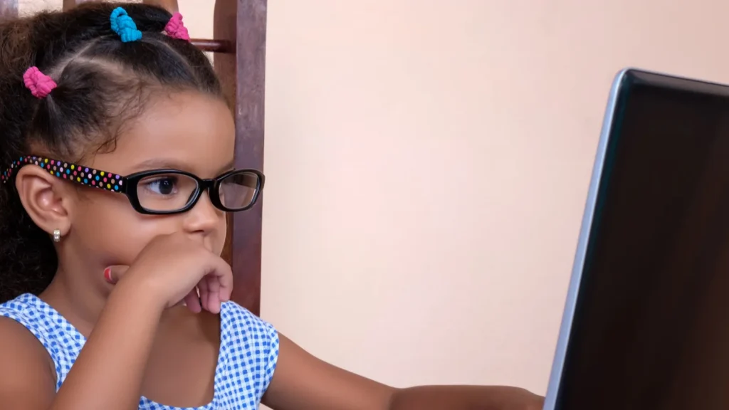 multiracial small girl wearing glasses and using a laptop comput