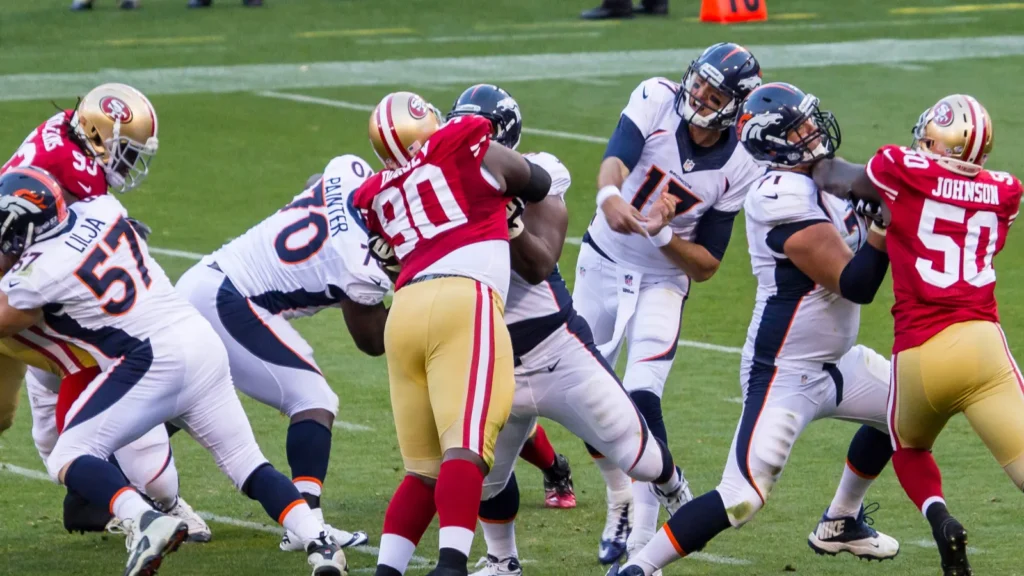 San Francisco 49ers and Denver Broncos players clash during an active play on a football field.