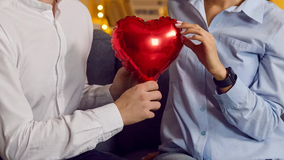 A man giving a heart shaped balloon to a woman