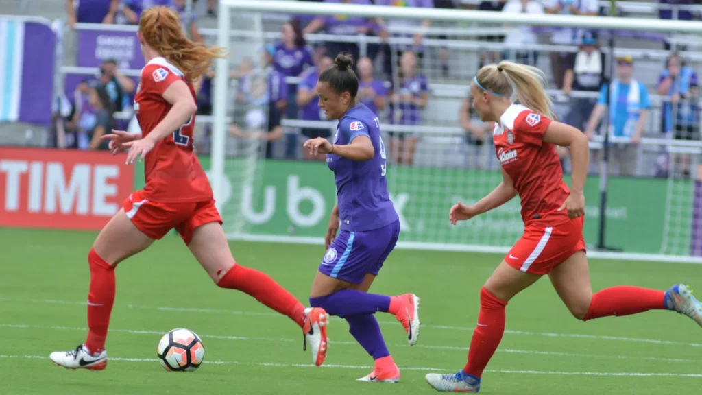 Women's soccer match in action with players wearing red and purple kits on the pitch.