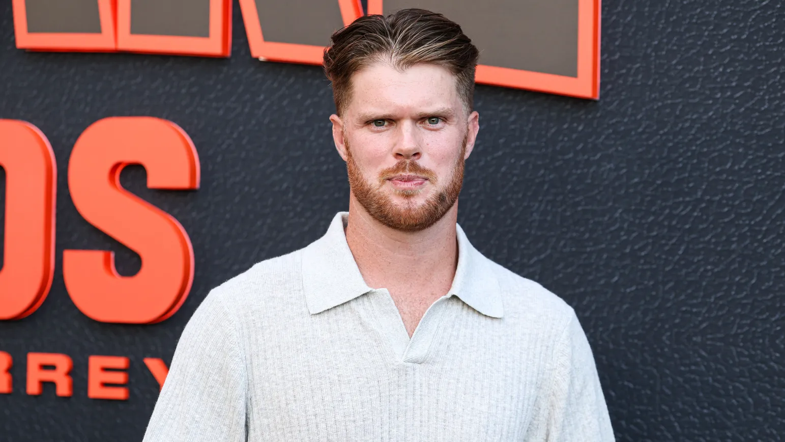 NFL quarterback Sam Darnold posing in a light polo shirt in front of an event backdrop.