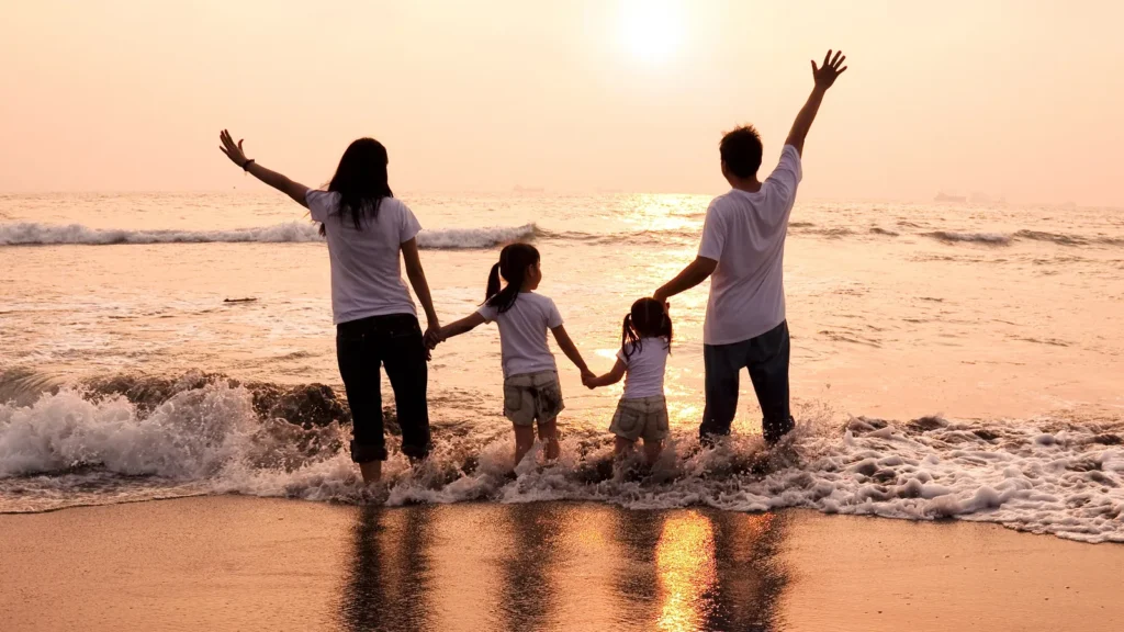 Happy family holding hands on a beach while watching the sunset