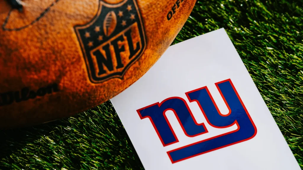 New York Giants logo and an American football ball on green grass.