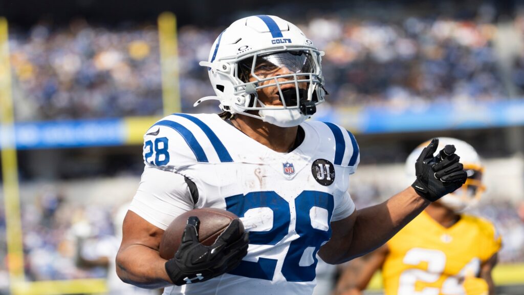 Jonathan Taylor wearing a white number 28 jersey, and holds the football in hand on the field