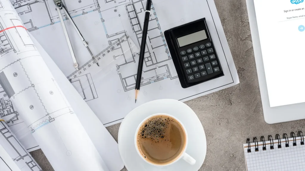 Top view of an architect's workplace with a coffee cup, blueprints and a calculator